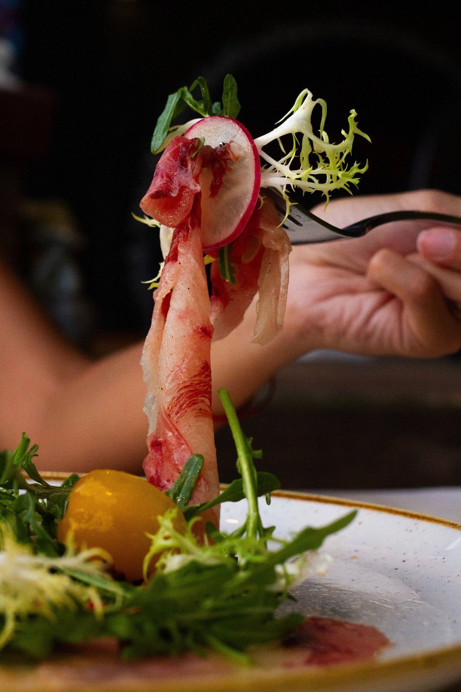 Forkful of fish carpaccio with frisée and radish